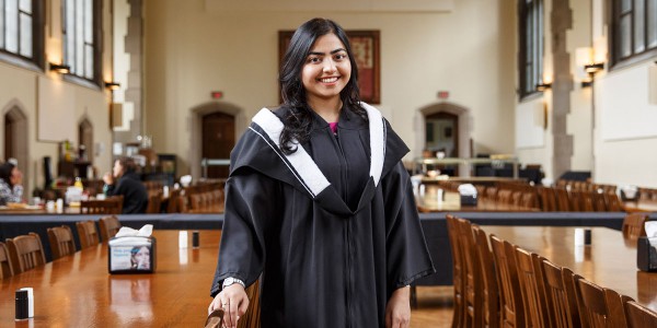 Vaneeza Moosa stands in Burwash Dining Hall in her graduation gown. 