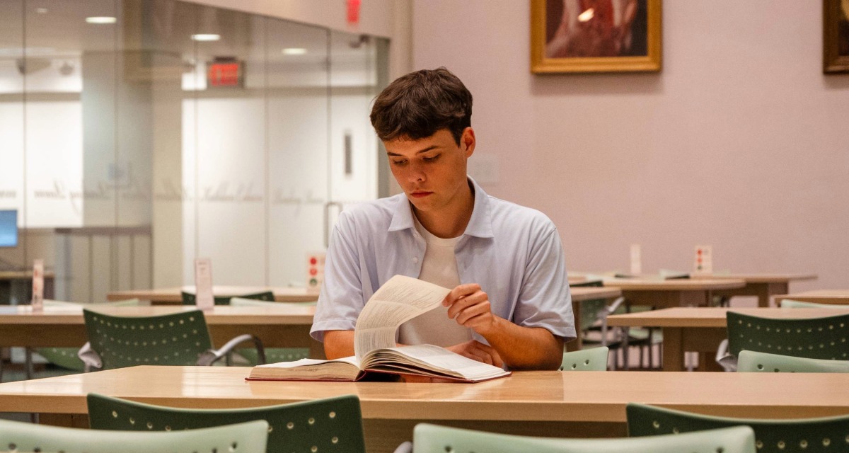Shane Joy turns the pages of a book while seated in E.J. Pratt Library on Victoria University campus.